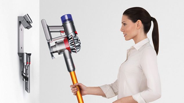 A woman placing a Dyson V8 vacuum cleaner back into its charging station
